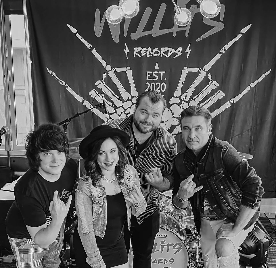 Willits Records, four members, in front of a backdrop reading WILLITS RECORDS EST. 2020 flanked by two skeleton hands throwing horns. A drum kit carrying the same logo stands behind them.